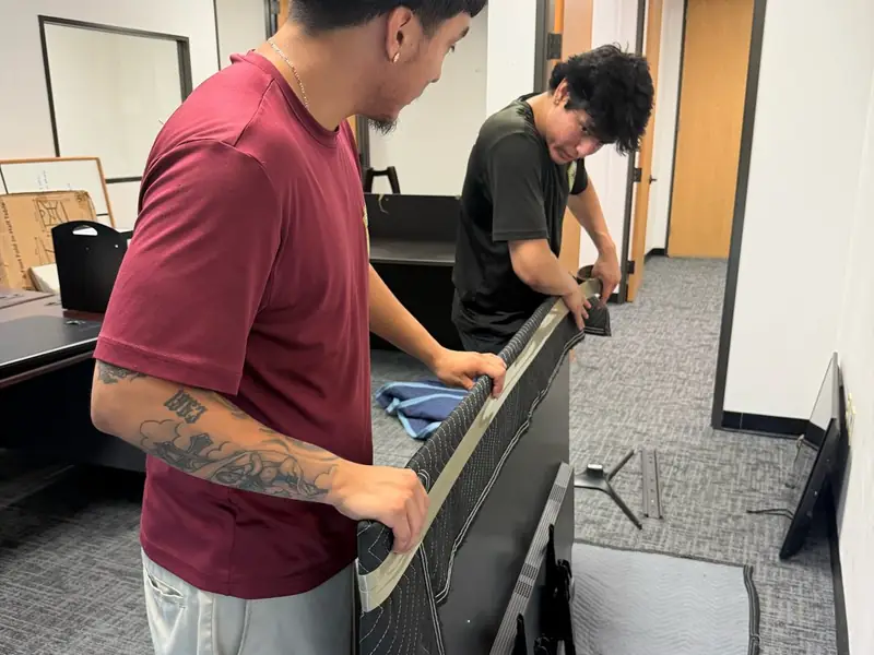 Two movers wrapping a large office TV during a commercial move