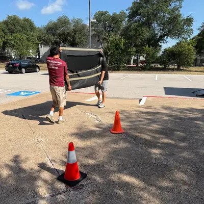 Two movers carrying a blanket-wrapped item across a parking lot to the truck