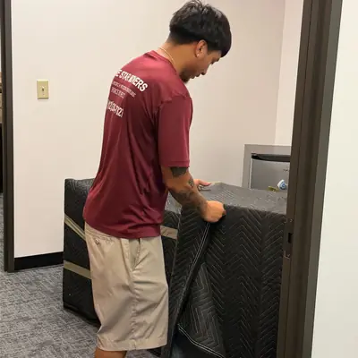 Mover in a maroon shirt wrapping office furniture in a moving pad