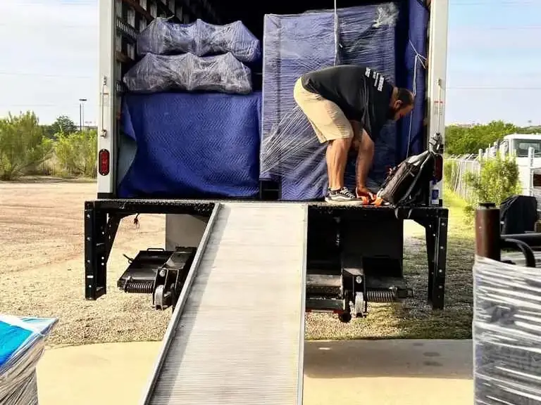 Mover securing a padded and shrink-wrapped load at the back of the truck, with the loading ramp down