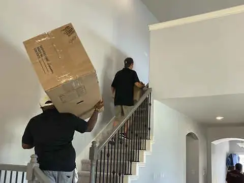 Mover carrying a large moving box up a staircase inside a home